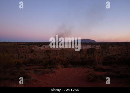 Dérives de fumée de feu d'herbe & Uluru au crépuscule avec l'installation d'art Field of Light de l'artiste Bruce Munro et fumée de feu d'herbe en Australie centrale Banque D'Images