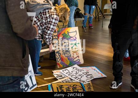 Photo d'une femme ramassant un panneau « Darkness Cannot Overcome Darkness » sur une pile de panneaux avant un événement Martin Luther King Jr. march. Banque D'Images