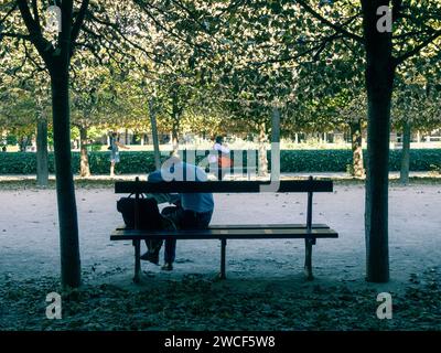 Un individu solitaire est assis sur un banc de parc, trempé dans la pensée ou peut-être profiter d'un moment de solitude, Palais Royal, Paris, France. Banque D'Images