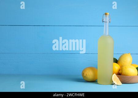 Bouteille de liqueur savoureuse de limoncello et citrons sur la table bleu clair, espace pour le texte Banque D'Images