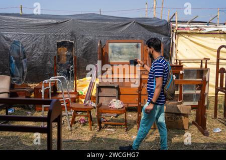 Jaynagar, Inde. 14 janvier 2024. Un homme passe devant un stock de meubles usagés tout en enregistrant une vidéo à l'intérieur d'une foire de la ferraille au Bengale occidental. Les habitants de Mathurapur Bengale occidental, en Inde, ont observé une bonne pratique de gestion des déchets en organisant une sorte de foire, la «Bhanga Mela» (Une foire des articles de rebut), où ils exposent des objets ménagers usagés et abandonnés à la vente. Des milliers de personnes viennent ici pour acheter ces produits de rebut ou des biens d'occasion pour les utiliser dans leurs maisons. Crédit : SOPA Images Limited/Alamy Live News Banque D'Images