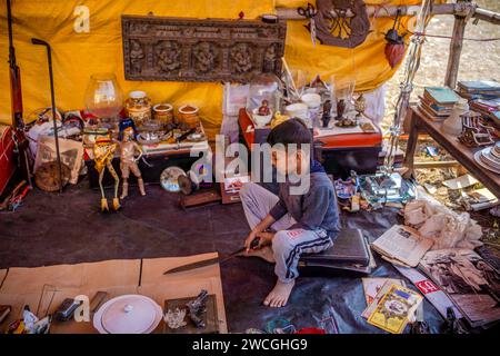 Jaynagar, Inde. 14 janvier 2024. Un petit garçon joue avec un poignard d'occasion à l'intérieur de la boutique de son père à une foire de la ferraille au Bengale occidental. Les habitants de Mathurapur Bengale occidental, en Inde, ont observé une bonne pratique de gestion des déchets en organisant une sorte de foire, la «Bhanga Mela» (Une foire des articles de rebut), où ils exposent des objets ménagers usagés et abandonnés à la vente. Des milliers de personnes viennent ici pour acheter ces produits de rebut ou des biens d'occasion pour les utiliser dans leurs maisons. Crédit : SOPA Images Limited/Alamy Live News Banque D'Images