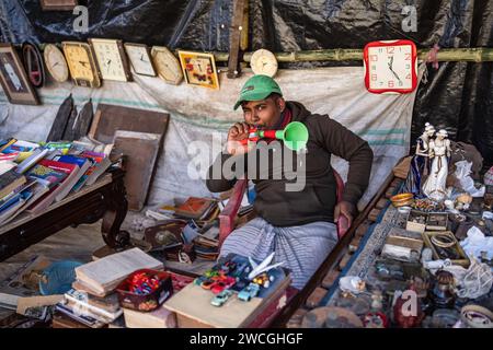 Jaynagar, Inde. 14 janvier 2024. Un garçon joue une flûte à jouets à l'intérieur d'un magasin de ferraille pour appeler des acheteurs dans une foire de ferraille au Bengale occidental. Les habitants de Mathurapur Bengale occidental, en Inde, ont observé une bonne pratique de gestion des déchets en organisant une sorte de foire, la «Bhanga Mela» (Une foire des articles de rebut), où ils exposent des objets ménagers usagés et abandonnés à la vente. Des milliers de personnes viennent ici pour acheter ces produits de rebut ou des biens d'occasion pour les utiliser dans leurs maisons. Crédit : SOPA Images Limited/Alamy Live News Banque D'Images