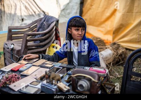 Jaynagar, Inde. 15 janvier 2024. Un garçon vend des gadgets électroniques d'occasion comme des téléphones portables et des appareils photo usagés dans une foire à la ferraille au Bengale occidental. Les habitants de Mathurapur Bengale occidental, en Inde, ont observé une bonne pratique de gestion des déchets en organisant une sorte de foire, la «Bhanga Mela» (Une foire des articles de rebut), où ils exposent des objets ménagers usagés et abandonnés à la vente. Des milliers de personnes viennent ici pour acheter ces produits de rebut ou des biens d'occasion pour les utiliser dans leurs maisons. Crédit : SOPA Images Limited/Alamy Live News Banque D'Images