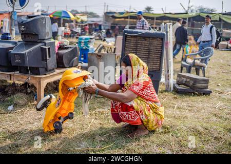 Jaynagar, Inde. 14 janvier 2024. Une femme lave un cycle de jouets usagés pour le vendre à une foire à la ferraille au Bengale occidental. Les habitants de Mathurapur Bengale occidental, en Inde, ont observé une bonne pratique de gestion des déchets en organisant une sorte de foire, la «Bhanga Mela» (Une foire des articles de rebut), où ils exposent des objets ménagers usagés et abandonnés à la vente. Des milliers de personnes viennent ici pour acheter ces produits de rebut ou des biens d'occasion pour les utiliser dans leurs maisons. Crédit : SOPA Images Limited/Alamy Live News Banque D'Images