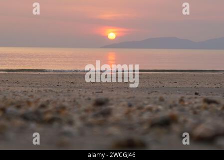 Coucher de soleil lumineux avec grand soleil jaune sous la surface de la mer. Reflet du coucher du soleil scintillant sur le rivage sablonneux. Fond de ciel d'été sur le coucher du soleil Banque D'Images