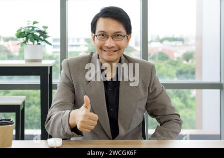 Un homme portant un costume formel sourit et montre un signe pouce vers le haut avec sa main pour exprimer son approbation. Banque D'Images