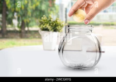 Les mains humaines mettent des pièces en dollars d'or dans des bocaux en verre sur la table. Concept d'épargne financière Banque D'Images