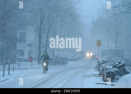 Hambourg, Allemagne. 16 janvier 2024. Un cycliste roule sur une route enneigée. L'hiver est de retour en Allemagne. La neige fraîche et les routes verglacées ont entraîné plusieurs accidents. Le tout clair pour les routes glacées n'est pas en vue pour le moment. Crédit : Marcus Brandt/dpa/Alamy Live News Banque D'Images