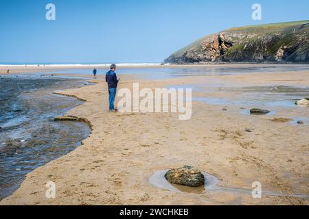 Un homme utilisant un téléphone portable se tenant sur la plage de Mawgan Porth à marée basse dans les Cornouailles au Royaume-Uni. Banque D'Images