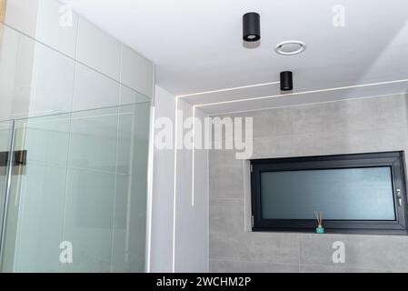 Bandes lumineuses LED montées dans le mur et le plafond dans une salle de bain moderne, anemostat de ventilation visible. Banque D'Images