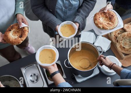 Gros plan des mains de volontaires donnant de la nourriture gratuite aux réfugiés du Moyen-Orient à la soupe populaire, espace de copie Banque D'Images