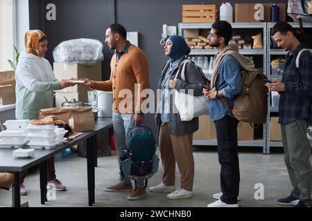 Vue latérale sur toute la longueur du groupe de personnes du Moyen-Orient debout dans la queue au centre d'aide aux réfugiés pour des repas chauds et des fournitures gratuites Banque D'Images