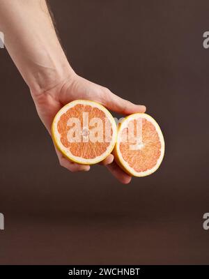 Deux moitiés d'un pamplemousse coupé sur la main de l'homme sur un fond brun. Banque D'Images