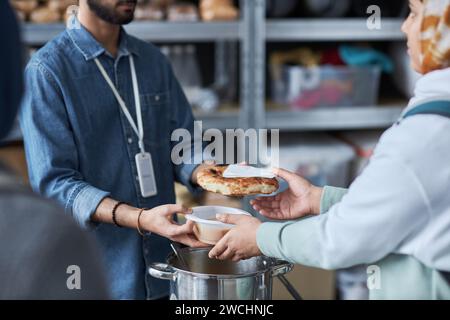 Gros plan d'un homme méconnaissable du Moyen-Orient aidant des réfugiés à la soupe populaire et distribuant des repas chauds Banque D'Images