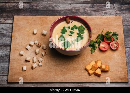 Soupe à la crème de citrouille végétale dans une assiette sur une planche à découper avec persil, tomates, tranches de citrouille et craquelins. Vue de dessus Banque D'Images