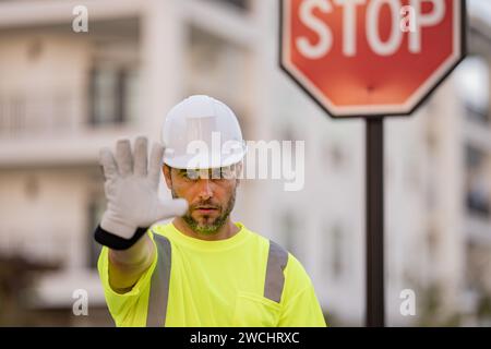 Homme en uniforme de travailleur et hardHat avec la main ouverte faisant signe d'arrêt avec l'expression sérieuse et confiante, geste de défense. Travailleur sérieux avec arrêt de route Banque D'Images