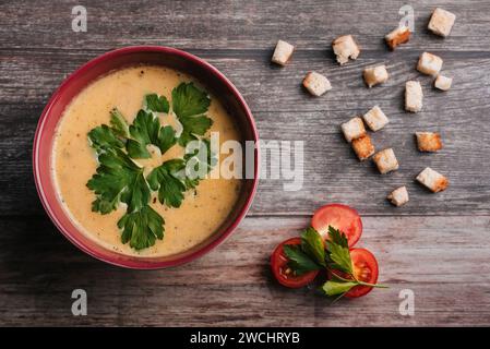 Soupe végétarienne à la crème de citrouille avec persil dans un bol sur une table en bois avec tomates et craquelins. Cuisine traditionnelle du village pour Halloween. T Banque D'Images