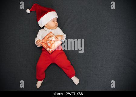 Garçon endormi dans le chapeau du Père Noël est couché avec une boîte cadeau dans sa main et une copie de l'espace Banque D'Images