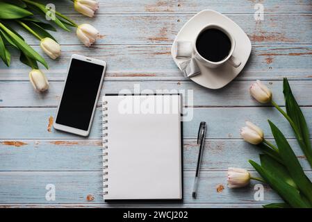Blancs de printemps d'un travail de freelance avec un bouquet de tulipes blanches, un smartphone, un bouquet blanc vide et une tasse de café dans ses mains sur un b Banque D'Images