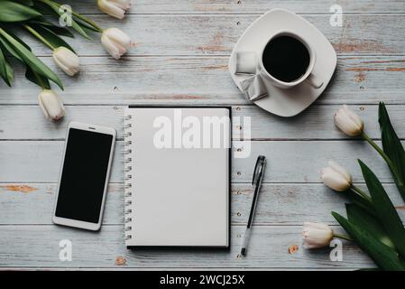 Blancs de printemps d'un travail de freelance avec un bouquet de tulipes blanches, un smartphone, un bouquet blanc vide et une tasse de café dans ses mains sur un b Banque D'Images