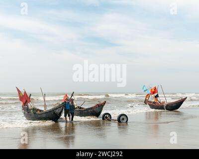 Pêcheurs à Sam son Beach, Thanh Hoa, Vietnam avec leurs bateaux à la plage à la fin de la journée de travail., prêts à les transporter plus loin sur la plage Banque D'Images