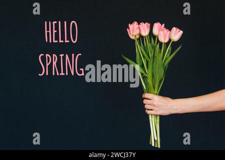 Carte de voeux avec l'inscription bonjour Spring. Bouquet de fleurs roses de tulipe dans la main d'une femme sur un fond avec un texte de félicitations Banque D'Images