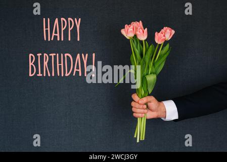 Bouquet de fleurs roses de tulipes dans la main d'un homme donnant. Carte de voeux avec texte joyeux anniversaire Banque D'Images