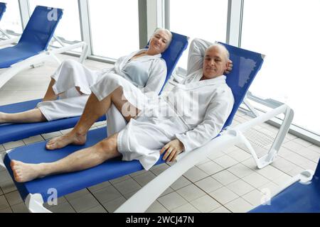 Une femme âgée avec un homme en peignoirs sur un transat près de la piscine. Détendez-vous dans le centre thermal. Banque D'Images