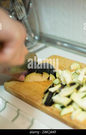 Homme caucasien coupant des aubergines sur une table en bois. Intérieur Banque D'Images