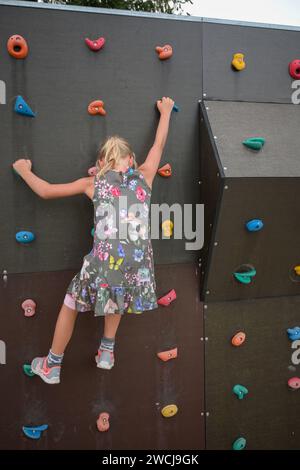 Une petite fille grimpe sur le terrain de jeu et sur le mur d'escalade. Banque D'Images