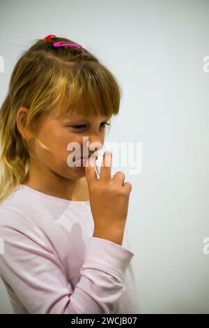 petite fille amère en pyjama vaporise son nez avec un spray anti-pneumonie - fond flou. Banque D'Images