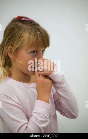 petite fille amère en pyjama vaporise son nez avec un spray anti-pneumonie - fond flou. Banque D'Images