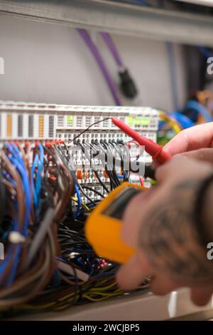 Un électricien travaillant dans une armoire électrique teste les câbles à l'aide d'un testeur. Banque D'Images