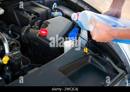 le mécanicien ajoute de l'eau aux lave-linge, en prenant soin de la voiture, en gros plan et en arrière-plan flou. Banque D'Images