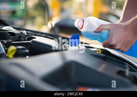 le mécanicien ajoute de l'eau aux lave-linge, en prenant soin de la voiture, en gros plan et en arrière-plan flou. Banque D'Images