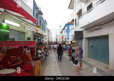 Vacanciers / touristes Walking & Standing sur l'étroite Rua Dr. Frederico Ramos Mendes (rue des bars) dans la soirée à Alvor, Algarve, Portugal, UE Banque D'Images