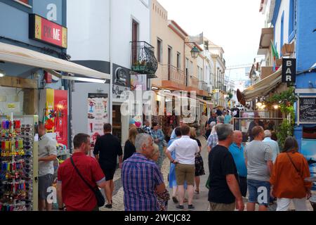 Vacanciers / touristes Walking & Standing sur l'étroite Rua Dr. Frederico Ramos Mendes (rue des bars) dans la soirée à Alvor, Algarve, Portugal, UE Banque D'Images