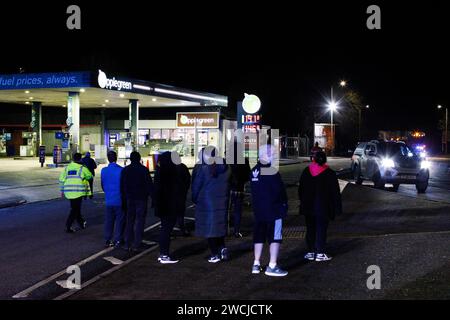 Merthyr Tydfil, Galles du Sud, Royaume-Uni. 15 janvier 2024. Un poids lourd de charge anormale a traversé le centre-ville lundi soir, après avoir été incapable de terminer son voyage à Hirwaun la nuit dernière à cause du mauvais temps. Le camion géant de 78m a été escorté par la police et les routes fermées pour permettre le passage du camion, ce qui a attiré une foule nombreuse qui l'a regardé passer. Crédit : Andrew Bartlett/Alamy Live News Banque D'Images