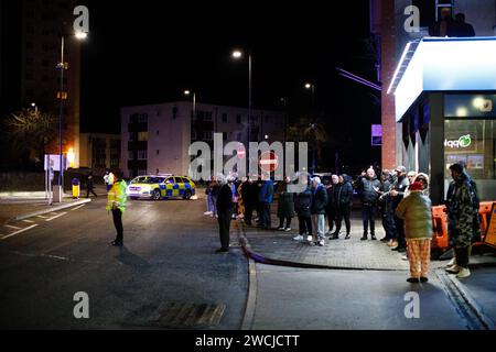 Merthyr Tydfil, Galles du Sud, Royaume-Uni. 15 janvier 2024. Un poids lourd de charge anormale a traversé le centre-ville lundi soir, après avoir été incapable de terminer son voyage à Hirwaun la nuit dernière à cause du mauvais temps. Le camion géant de 78m a été escorté par la police et les routes fermées pour permettre le passage du camion, ce qui a attiré une foule nombreuse qui l'a regardé passer. Crédit : Andrew Bartlett/Alamy Live News Banque D'Images