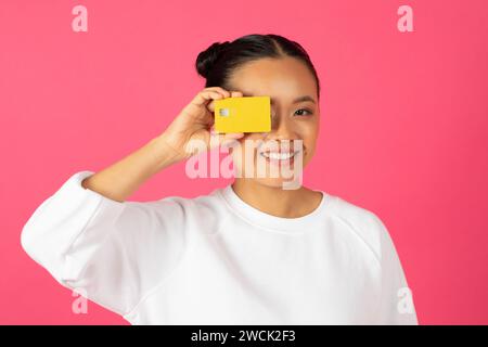 Paiements faciles. Joyeuse jeune femme asiatique couvrant l'œil avec carte de crédit Banque D'Images