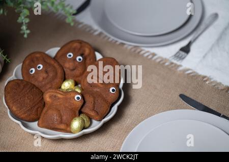 Gros plan de muffins de Pâques en forme de lapins et d'œufs avec des yeux, œufs en chocolat sur la table servie Banque D'Images