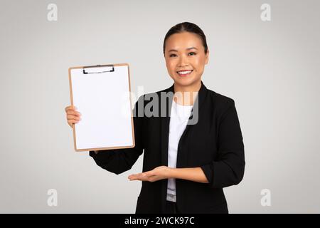 Femme d'affaires asiatique confiante dans un costume noir présentant un presse-papiers vierge avec espace de copie Banque D'Images