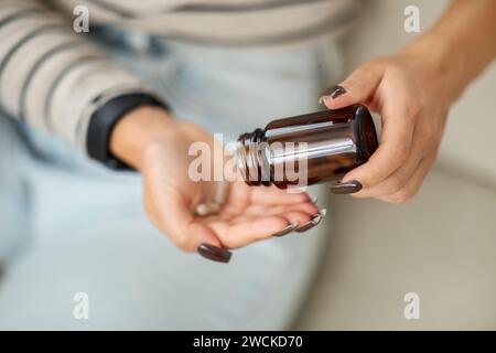 Gros plan des mains d'une femme qui distribue soigneusement des médicaments à partir d'une bouteille brune Banque D'Images