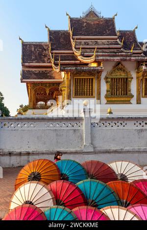 Petite fille marchant derrière des parapluies devant le temple du Palais Royal (Haw Pha Bang) à Luang Prabang, Laos Banque D'Images