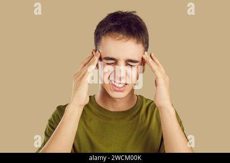 Portrait d'un jeune garçon souffrant de maux de tête isolé sur un fond beige studio. Banque D'Images