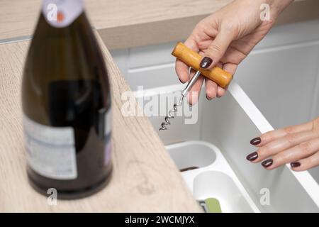 femme tient un tire-bouchon dans sa main pour ouvrir une bouteille de vin. la main d'une femme prend un tire-bouchon dans un tiroir de cuisine. alcoolisme féminin Banque D'Images