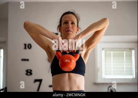 FIT jeune femme travaillant à la maison en soulevant un poids kettlebell de 8 kg. Banque D'Images