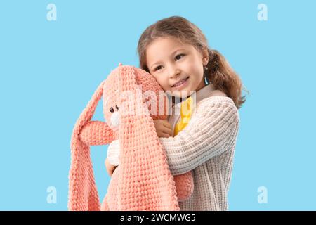 Jolie petite fille avec ruban jaune et lapin jouet sur fond bleu. Concept de sensibilisation au cancer de l'enfant Banque D'Images