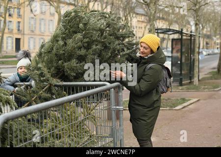 Mère et fille jettent les arbres de Noël derrière la clôture au recyclage en France Banque D'Images